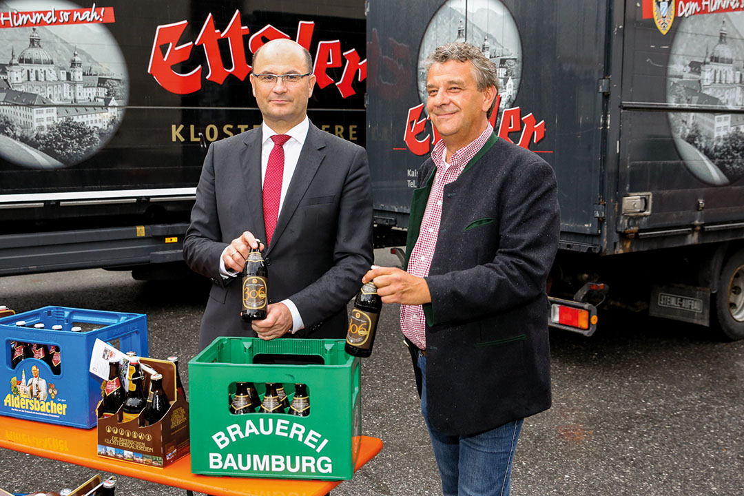 Braumeister Andreas Goblirsch (rechts) präsentiert dem Heimat- und Finanzminister Albert Füracker den Beitrag der Klosterbrauerei Baumburg zur Jubiläumsausgabe. 